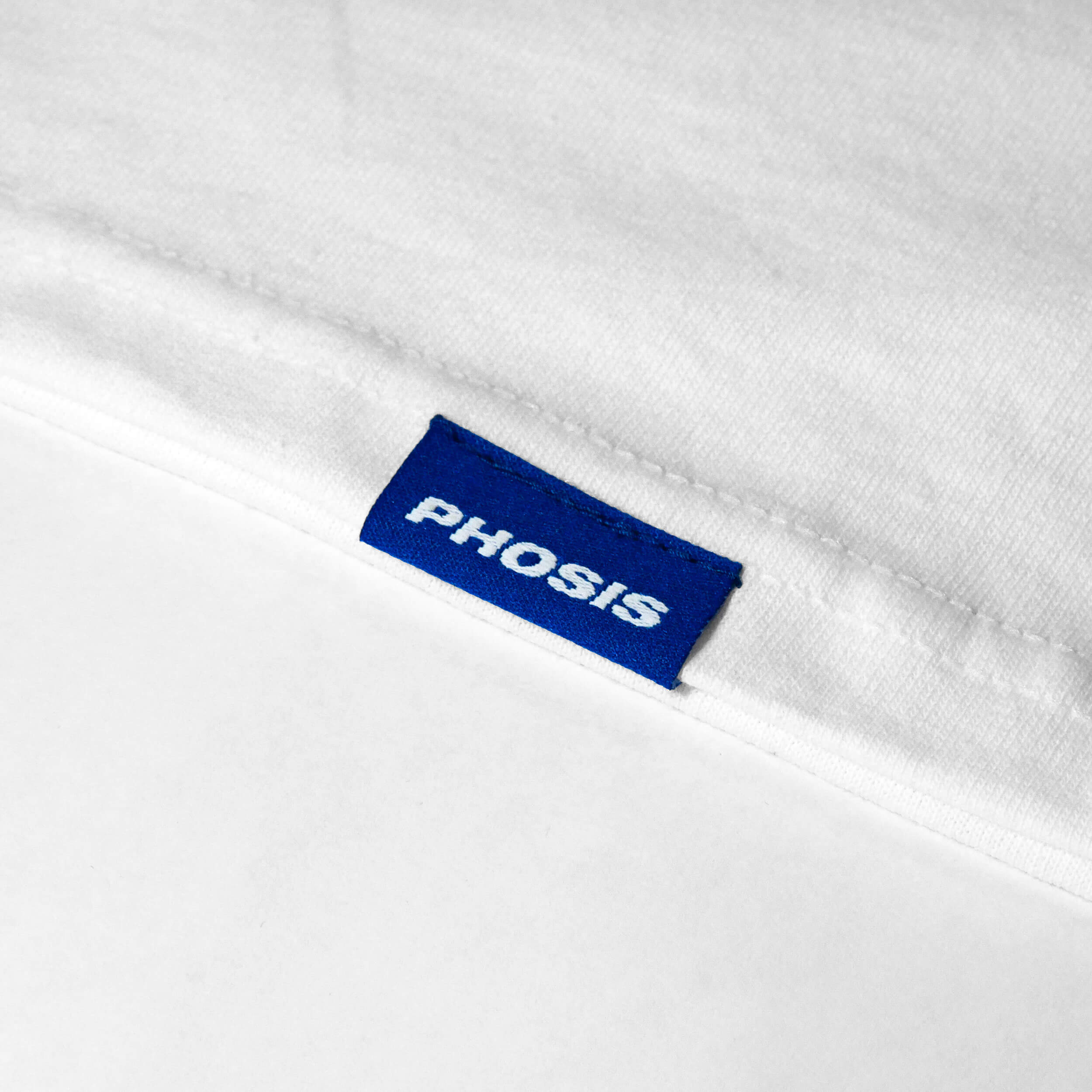 Close up view of the blue woven label in the WEEPING GHOST white t-shirt from PHOSIS Clothing