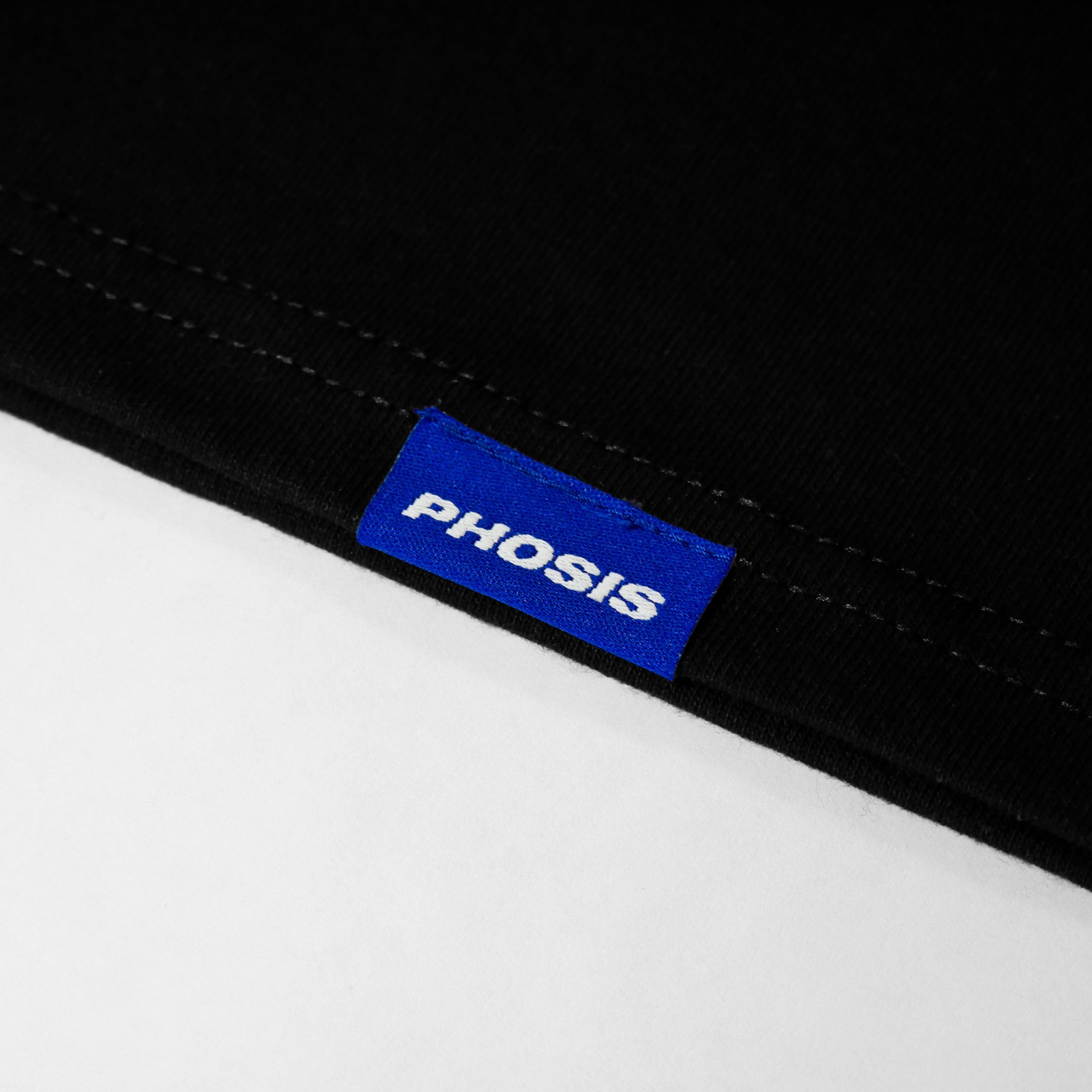 Close up view of the blue woven label in the BABYLON black long sleeve from PHOSIS® Clothing