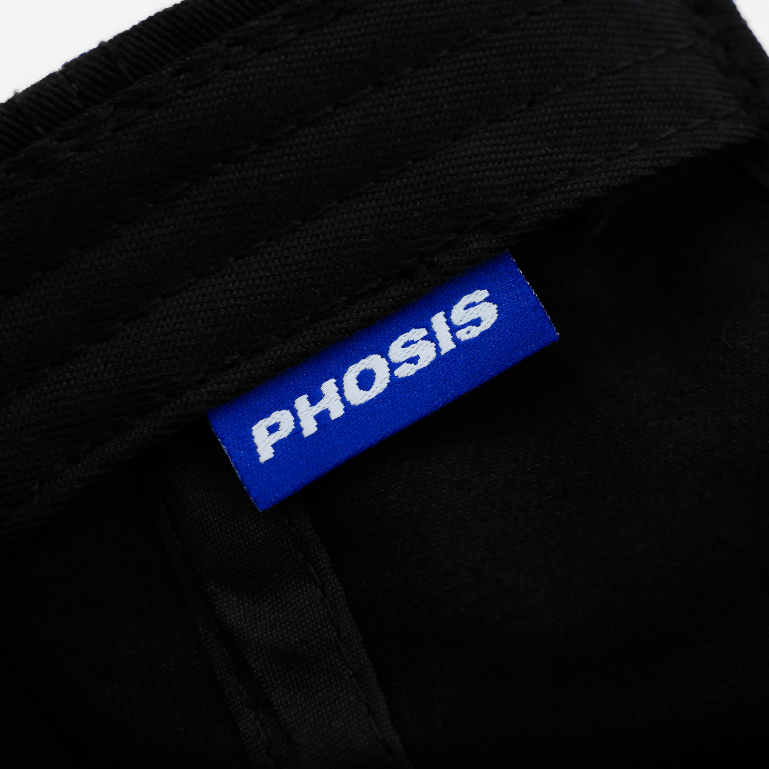 Close up view of the woven label in the Barbed Wire black dad hat from PHOSIS Clothing