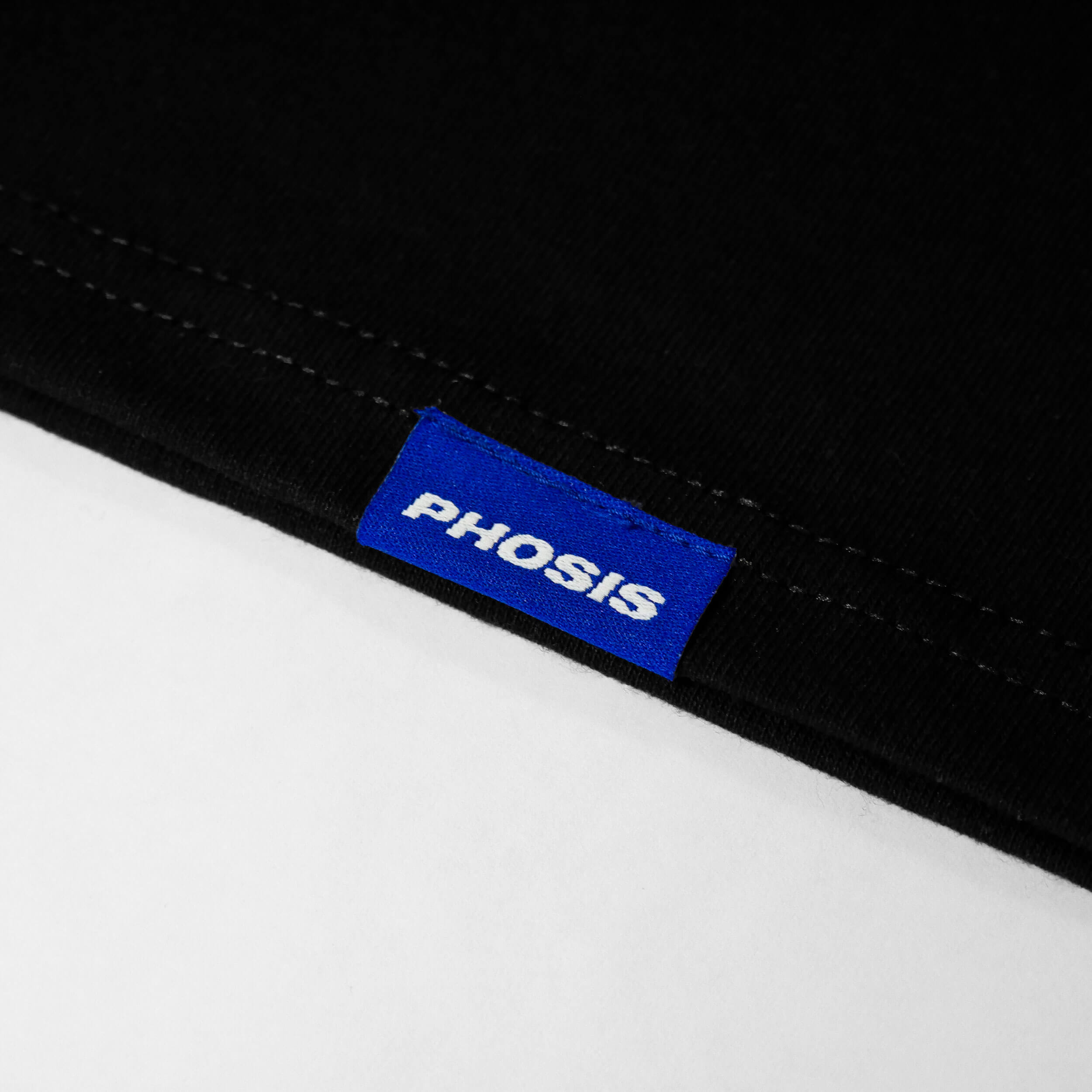 Close up view of the blue woven label in the ATLANTIC black long sleeve from PHOSIS Clothing
