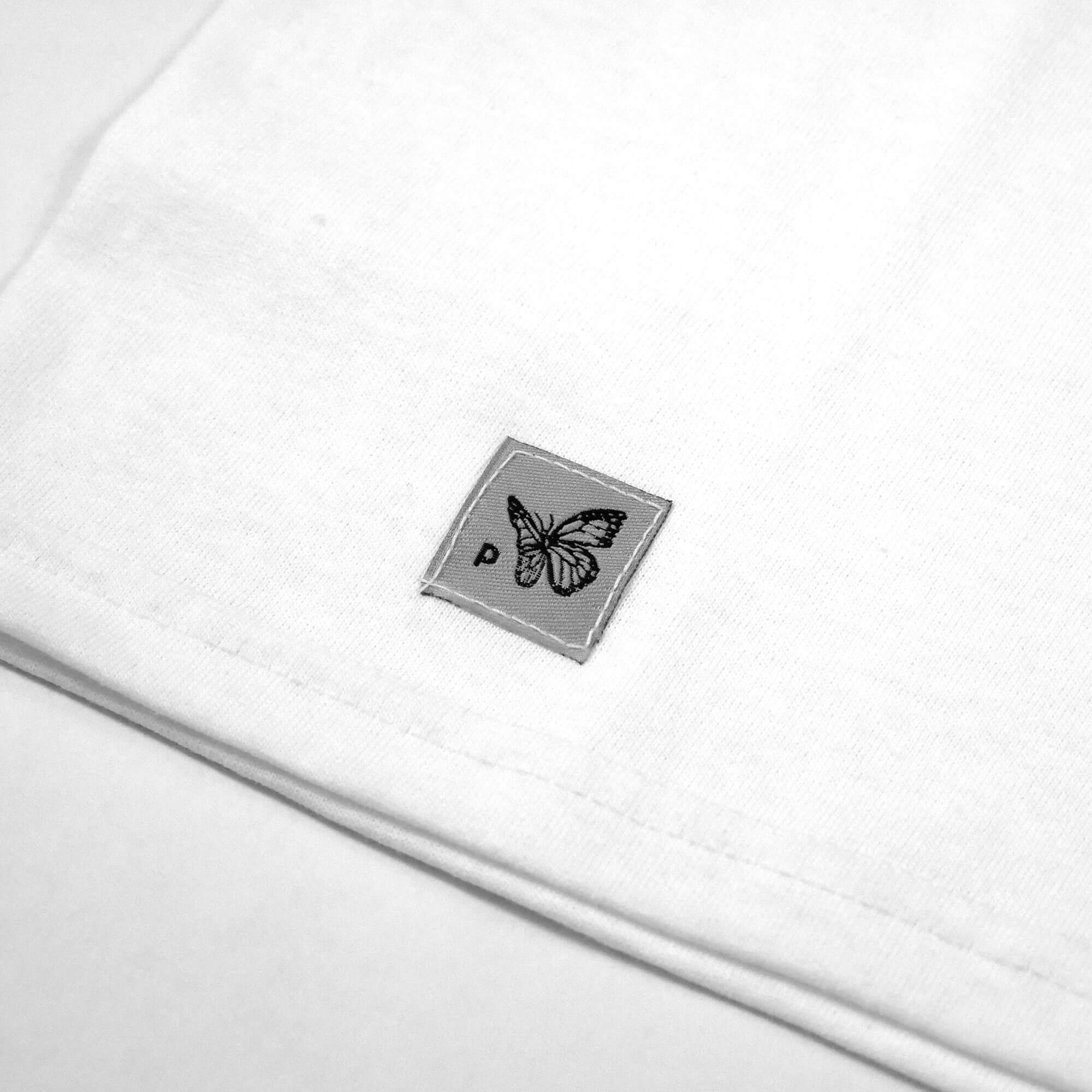 Close up view of the grey logo tag in the VOYAGER white t-shirt from PHOSIS Clothing